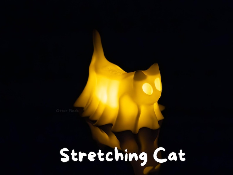 Pode incluir: Uma l&acirc;mpada amarela brilhante em forma de gato com um corpo transl&uacute;cido drapeado e uma cauda ereta. A figura apresenta dois recortes ovais para os olhos e est&aacute; posicionada contra um fundo escuro. O texto "Stretching Cat" aparece na base.