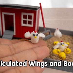 Puede incluir: Un gallinero en miniatura rojo y blanco con base gris, un rastrillo de mango rojo y varias figuras peque&ntilde;as de pollos blancos y amarillos. Una figura de pollo blanco con alas y cuerpo articulados se sostiene en primer plano.