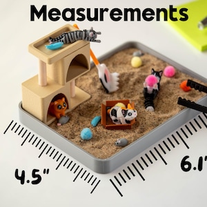 May include: A miniature cat-themed sandbox with a beige cat tower, sand, and various cat figurines. The sandbox measures 4.5 inches by 6.1 inches. Includes a small rake and tweezers.