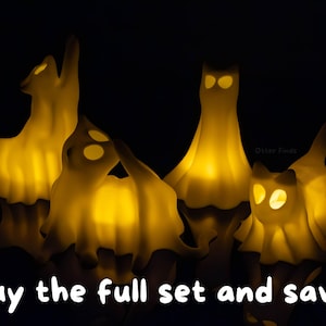 Pode incluir: Quatro figuras de fantasmas em forma de gato, em tom esbranqui&ccedil;ado, com olhos e corpos amarelos iluminados contra um fundo preto. As figuras apresentam v&aacute;rias poses, incluindo sentadas e esticadas. O texto "Buy the full set and save!" est&aacute; na parte inferior.