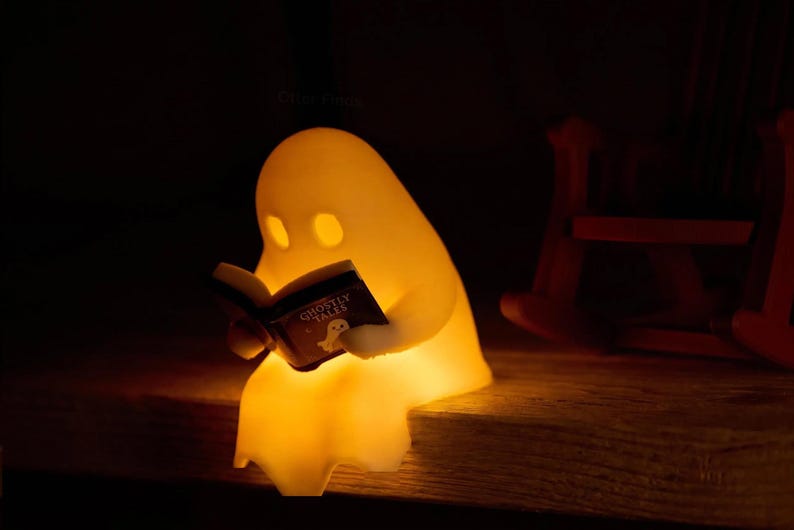 Glowing reading ghost perched on the edge of a wooden bookshelf, holding its open black book, with the empty brown rocking chair positioned behind it to the right.