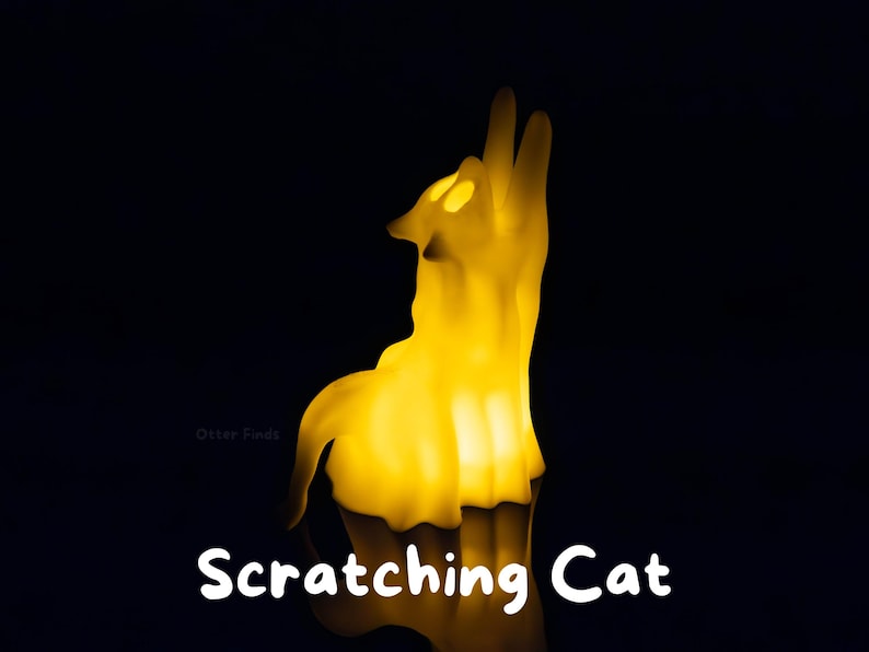 Pode incluir: Uma l&acirc;mpada amarela brilhante em forma de gato com um corpo transl&uacute;cido, representada numa posi&ccedil;&atilde;o sentada com a cabe&ccedil;a inclinada para cima. A luz emite um brilho quente e suave contra um fundo escuro. O texto "Scratching Cat" est&aacute; impresso em branco.