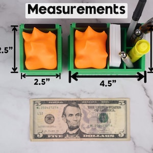 Puede incluir: Organizador de escritorio verde con dos compartimentos, cada uno de 6,35 cm por 6,35 cm. El organizador tiene 11,43 cm de ancho. Los compartimentos contienen objetos naranjas y amarillos.