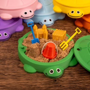 May include: Colorful turtle-shaped sandboxes with smiling faces. Each sandbox is filled with sand and miniature toys, including a bucket, shovel, and rake. The sandboxes are in various colors: green, purple, pink, blue, yellow, and orange.