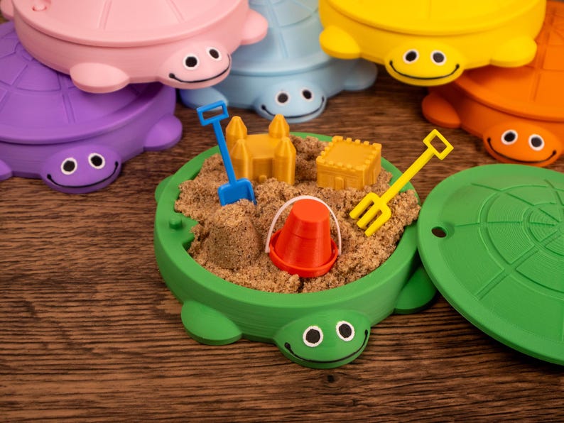 May include: Colorful turtle-shaped sandboxes with smiling faces. Each sandbox is filled with sand and miniature toys, including a bucket, shovel, and rake. The sandboxes are in various colors: green, purple, pink, blue, yellow, and orange.