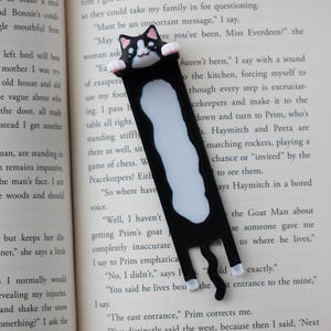 May include: A black and white cat bookmark. The bookmark depicts a black cat with white markings and a smiling face. The cat is holding onto the top of the pages. A fun accessory for book lovers.