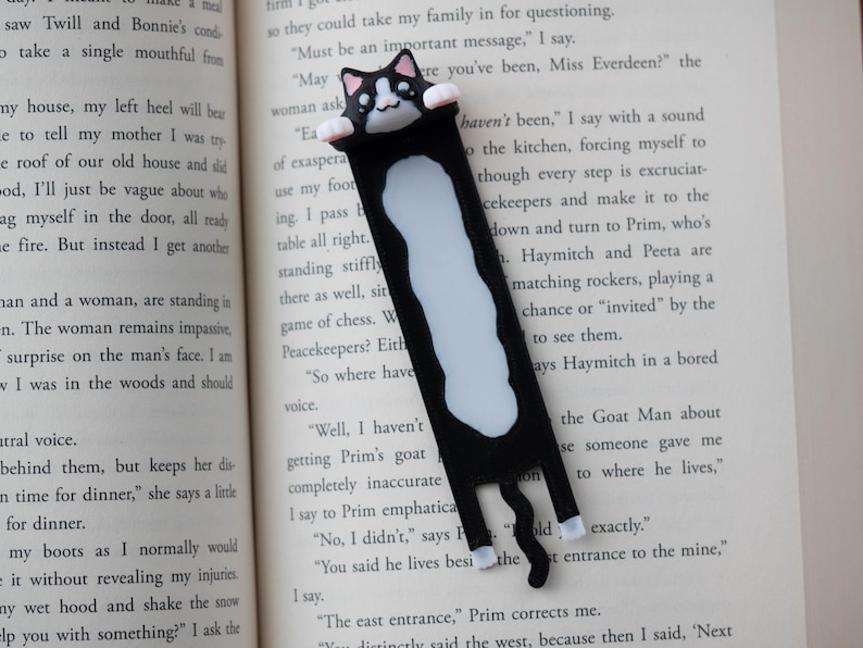 May include: A black and white cat bookmark. The bookmark depicts a black cat with white markings and a smiling face. The cat is holding onto the top of the pages. A fun accessory for book lovers.