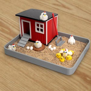 Puede incluir: Un gallinero en miniatura rojo y blanco con techo negro se encuentra en una bandeja rectangular gris llena de arena. El conjunto incluye varias figuras peque&ntilde;as de gallinas blancas, pollitos amarillos, huevos y un rastrillo rojo.
