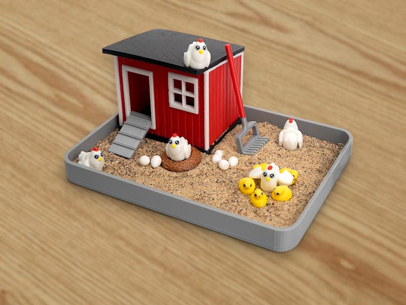 Puede incluir: Un gallinero en miniatura rojo y blanco con techo negro se encuentra en una bandeja rectangular gris llena de arena. El conjunto incluye varias figuras peque&ntilde;as de gallinas blancas, pollitos amarillos, huevos y un rastrillo rojo.