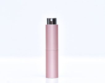 May include: A cylindrical, rose-gold perfume atomizer with a silver spray nozzle. The atomizer is divided into two sections and stands upright against a white background. The design is sleek and minimalist.