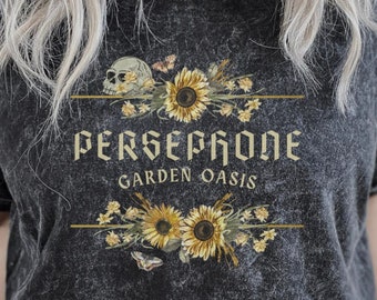May include: Black t-shirt with a distressed look featuring a graphic of a skull with sunflowers and the text "Persephone Garden Oasis".