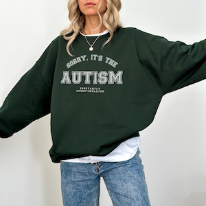 Könnte beinhalten: Ein dunkelgrüner Pullover mit dem Text "Sorry, it's the Autism Constantly Overstimulated" in weißen Buchstaben.