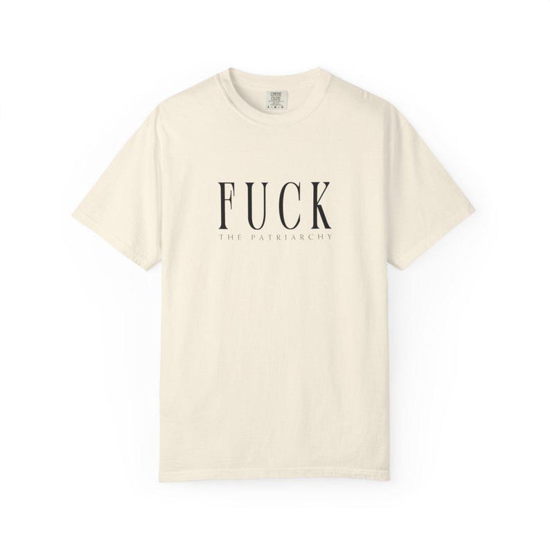 May include: Cream-colored t-shirt with the text "FUCK THE PATRIARCHY" in black, centered on the front. The text is in a bold, sans-serif font. The shirt has a crew neck and short sleeves.