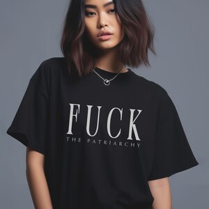 May include: Black t-shirt with the text "FUCK THE PATRIARCHY" in white, featuring a round neckline and short sleeves. The shirt is worn by a person with dark hair and a silver necklace.