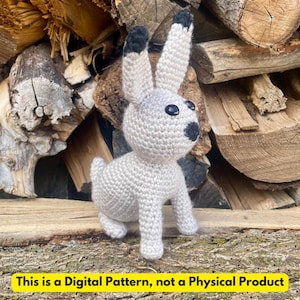 May include: A crocheted bunny rabbit in light gray yarn with black accents on the ears and nose. The bunny has black button eyes and is sitting on a wooden surface. The text at the bottom reads: "This is a Digital Pattern, not a Physical Product."