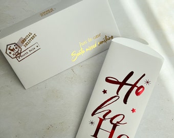 May include: Two white paper envelopes. The horizontal envelope features a gold foil stamp reading "Special Delivery North Pole" with a reindeer icon and "Just in case Santa missed something." The vertical envelope has red foil "Ho ho Ho" text.
