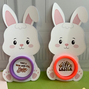 May include: Two white bunny shaped Easter decorations with a purple and orange circle with gold text. The purple circle says "Have a Won-Doh-Ful Easter" and the orange circle says "Happy Easter".