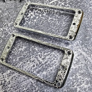 May include: Two chrome-plated guitar pickup rings with an ornate floral design. The rings are rectangular and have rounded corners.