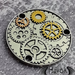 Könnte beinhalten: Ein kreisförmiges Design aus silbernen und goldenen Zahnrädern aus Metall. Die Zahnräder sind ineinandergreifend und haben eine Steampunk-Ästhetik.