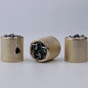 Könnte beinhalten: Drei goldfarbene Metallknöpfe mit einer strukturierten Oberfläche. Der mittlere Knopf hat ein schwarzes und grünes Design mit einer Sternform und einem Muster aus kleinen schwarzen Punkten. Die anderen beiden Knöpfe haben ein Muster aus kleinen schwarzen Punkten.