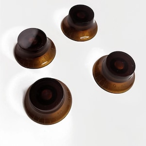 May include: Four brown guitar knobs with black centers and white numbers. The numbers on the knobs are 6, 9, 10, and 16.