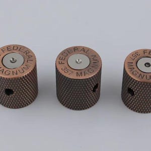 Puede incluir: Tres botones de guitarra de color cobre con una superficie texturizada. Cada botón presenta un centro plateado con el texto "FEDERAL 357 MAGNUM" grabado alrededor del borde.