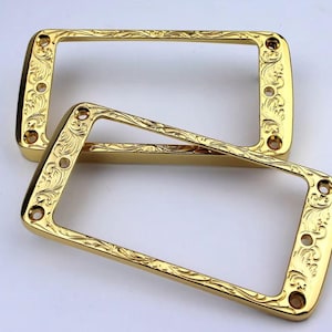 May include: Two gold-coloured guitar pickup rings with an ornate engraved design.