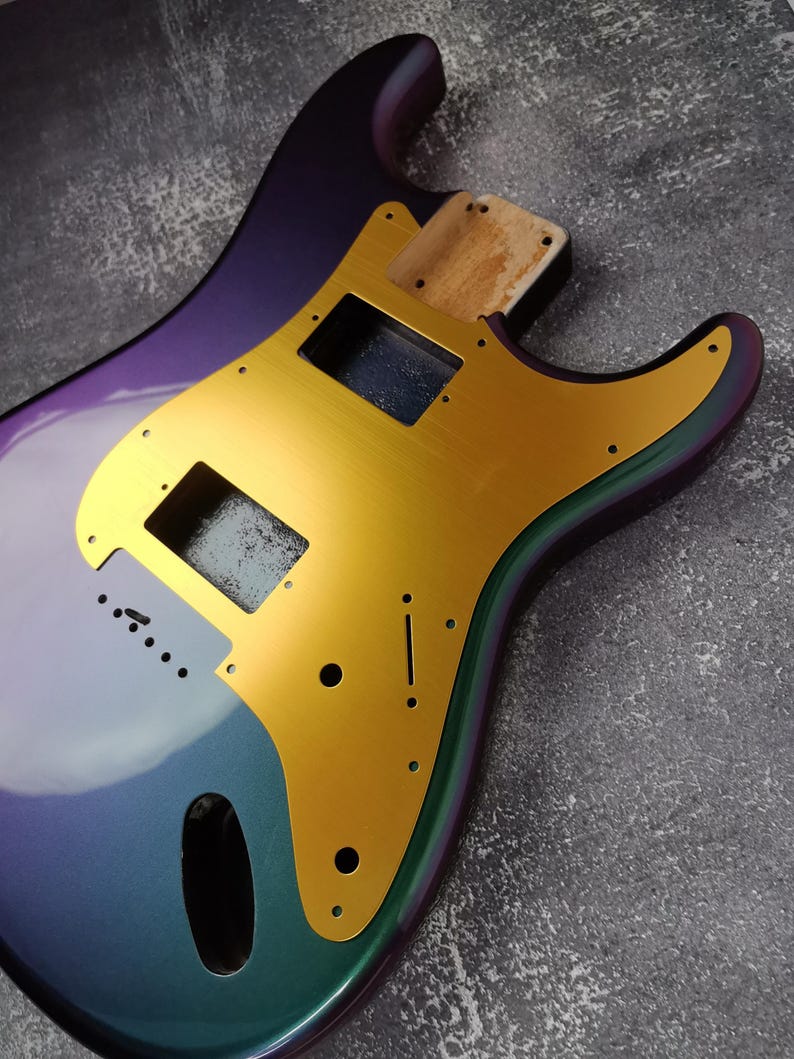 May include: A purple, green, and gold electric guitar body. The body is made of wood and has a gold pickguard.