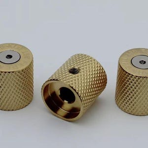 May include: Three gold-coloured metal knobs with a knurled texture and a silver centre. The knobs have a raised rim around the centre.