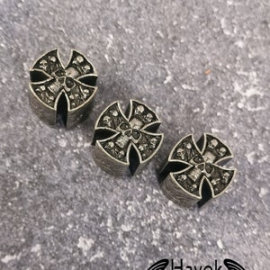 May include: Three silver metal guitar knobs with a skull and crossbones design. The knobs are round and have a raised design. The background is a grey textured surface. Havok Custom Guitars.