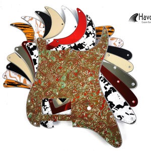 May include: A collection of guitar pickguards in various colours and patterns, including a green and gold swirl pickguard, a black and white pickguard, and a red pickguard. The pickguards are made by Havok Custom Guitars.