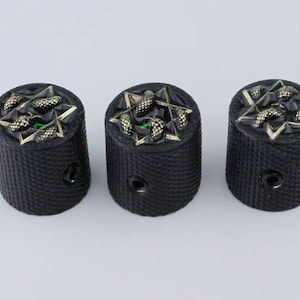 以下が含まれることがあります： 金と緑の星形のデザインが施された黒いギターノブが3つ。ノブはテクスチャ加工された表面をしています。