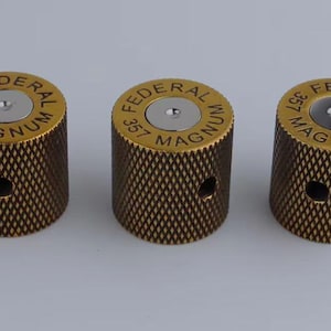 May include: Three gold-colored metal knobs with a textured surface. Each knob has a silver-colored center and the text "FEDERAL 357 MAGNUM" printed around the center.