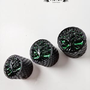 Puede incluir: Tres pomos de guitarra negros con un diseño de árbol verde. Los pomos son redondos y tienen una superficie texturizada. El texto "Havok Custom Guitars" es visible en la esquina superior derecha de la imagen.