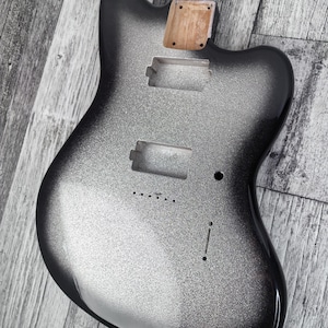 Pode incluir: Um corpo de guitarra elétrica prateado e preto com um acabamento brilhante. O corpo tem recortes para captadores e controles, e um encaixe para o braço de madeira. O corpo da guitarra é de cor sólida com um acabamento brilhante.