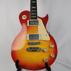 Può includere: Una chitarra elettrica rossa, arancione e gialla con un battipenna nero e hardware cromato. La chitarra è su un supporto nero.