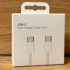 Könnte beinhalten: Weiße Verpackung für ein USB-C 60W Ladekabel (1 m) mit zwei weißen Kabeln und silbernen Steckern.