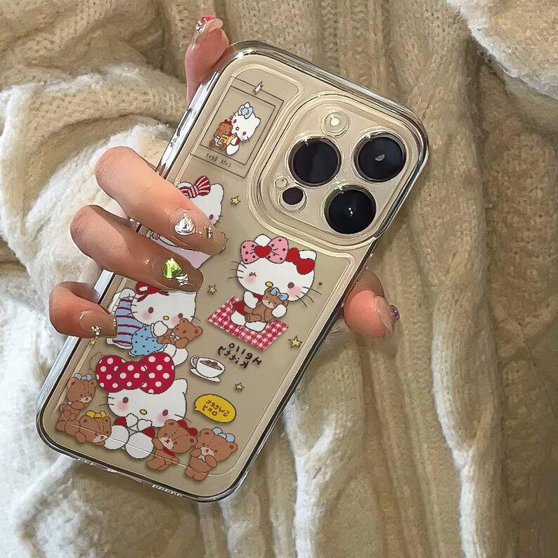 Peut inclure: Coque de t&eacute;l&eacute;phone transparente orn&eacute;e de motifs Hello Kitty et ours en peluche. L'&eacute;tui a un fond beige avec diverses images de Hello Kitty avec des n&oelig;uds rouges et des ours en peluche. L'&eacute;tui a une bordure transparente et recouvre l'appareil photo du t&eacute;l&eacute;phone.