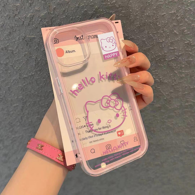 May include: A clear and pink phone case featuring a Hello Kitty design. The case has the words "hello kitty" and a Hello Kitty graphic. The case also has Instagram-themed elements and the word "HAPPY".