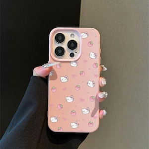 Może przedstawiać: R&oacute;żowe etui na telefon z powtarzającym się wzorem twarzy Hello Kitty, truskawek i kokardek. Etui ma teksturowaną powierzchnię i wycięcie na aparat. Projekt jest w uroczym i zabawnym stylu.