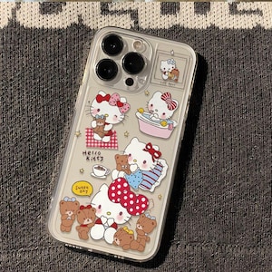 Peut inclure: Coque de t&eacute;l&eacute;phone transparente orn&eacute;e de motifs Hello Kitty et d'ours en peluche. La coque pr&eacute;sente diverses illustrations, dont Hello Kitty avec un n&oelig;ud rouge, tenant un ours en peluche et dans un bain. La coque porte &eacute;galement les mots "Hello Kitty" et "Sweet Day".