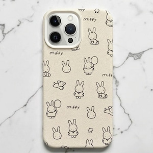 Puede incluir: Una funda para smartphone de color crema con un patrón repetitivo de líneas negras del conejo Miffy en varias poses, incluyendo globos y el texto "miffy" disperso por la superficie. La funda tiene un recorte para un sistema de triple cámara.