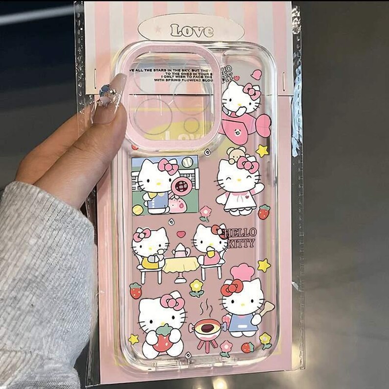 May include: Clear phone case with a pink border featuring Hello Kitty illustrations. The case has various images of Hello Kitty in different poses, along with strawberries and stars. The text "HELLO KITTY" is also visible.