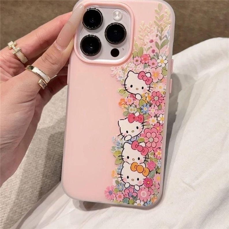 Puede incluir: Funda de tel&eacute;fono rosa con personajes de Hello Kitty y dise&ntilde;os florales. La funda tiene un borde transparente y un fondo rosa claro. Los personajes de Hello Kitty est&aacute;n rodeados de flores rosas, blancas y azules.