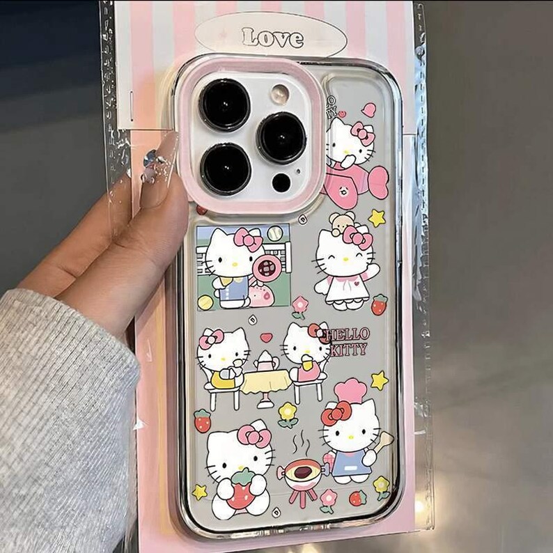 May include: Clear phone case featuring Hello Kitty illustrations in various poses with pink accents. The case has a pink border around the camera and the text "Hello Kitty". The packaging has the word "Love" at the top.