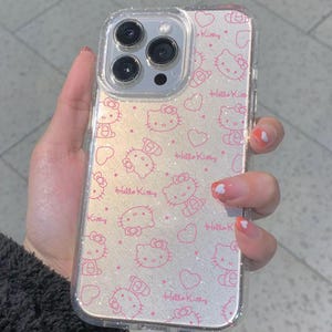 K&ouml;nnte beinhalten: Transparente Handyh&uuml;lle mit einem rosa Hello Kitty Muster und Herzen. Die H&uuml;lle hat einen glitzernden Hintergrund und die Worte "Hello Kitty" sind aufgedruckt. Die Handyh&uuml;lle ist f&uuml;r ein Smartphone konzipiert.