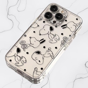 May include: A clear smartphone case featuring a repeating pattern of black and white Snoopy character illustrations and small black polka dots. The case has a rectangular cutout for a triple-lens camera system and a flash on the upper left corner.