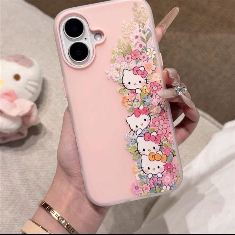 Puede incluir: Funda de tel&eacute;fono rosa con personajes de Hello Kitty y detalles florales. El dise&ntilde;o presenta caras de Hello Kitty con lazos, rodeadas de flores y hojas coloridas.