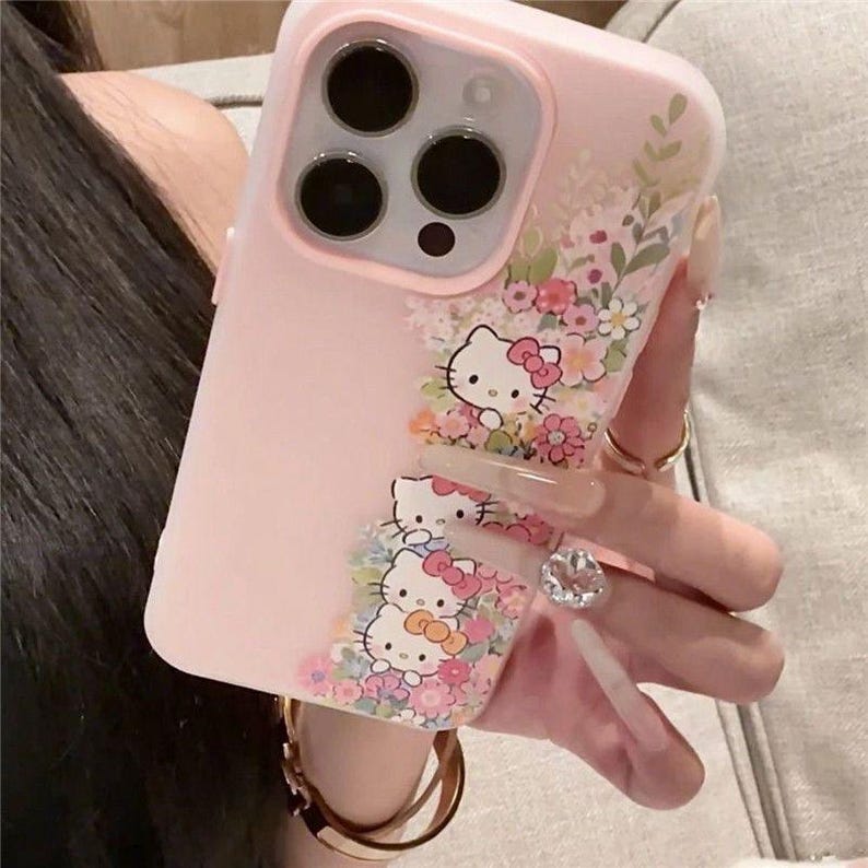 Puede incluir: Funda de tel&eacute;fono rosa con personajes de Hello Kitty y detalles florales. La funda tiene una secci&oacute;n transparente con purpurina flotante y peque&ntilde;as flores. El dise&ntilde;o incluye un soporte para anillos con una gema grande y transparente.