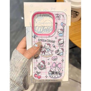 Puede incluir: Funda transparente para tel&eacute;fono con borde rosa, decorada con personajes de Hello Kitty e ilustraciones tem&aacute;ticas. La funda tiene un patr&oacute;n de cuadr&iacute;cula e incluye el texto "Hello Kitty" y "Welcome".